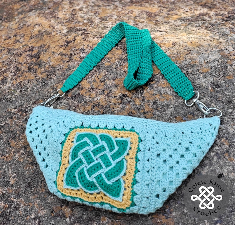 May include: A crocheted light blue bag with a green Celtic knot design. The bag has a green adjustable strap and a silver clasp. The bag is on a brown and gray textured surface. The text "Celtic Knot Crochet" is visible in the lower right corner of the image.