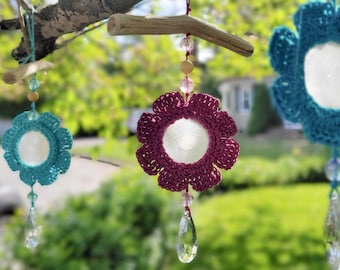 May include: Three crocheted flower ornaments hanging from a driftwood branch. The flowers are teal, pink, and turquoise. Each flower has a white circle in the center and is accented with crystal beads and a crystal drop.