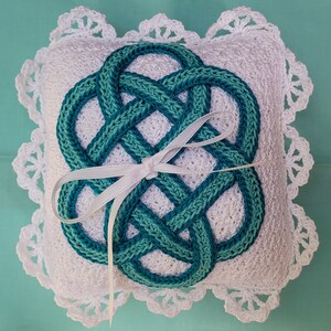 May include: White crocheted pillow with a teal Celtic knot design and a white satin ribbon.