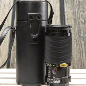 May include: A black camera lens with a black leather carrying case. The lens has a zoom range of 80-200mm and a maximum aperture of f/5.6-4.5. The lens has a depth of field scale and a focus ring. The lens is in good condition.