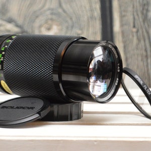 May include: A black camera lens with a 55-200mm zoom range and a 1:4.5 aperture. The lens has a black lens cap and a black filter attached to the front.