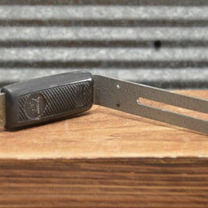 May include: A black and silver camera flash bracket with a textured grip. The bracket is designed to attach a flash to a camera.