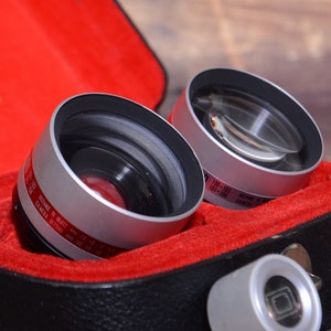 May include: Two silver and black camera lens attachments in a red velvet lined case. The lens attachments are labeled "100-103" and "101-104".
