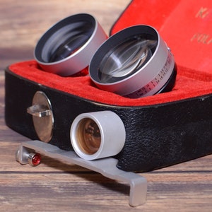 May include: A set of three silver camera lenses in a black and red leather case. The lenses are labeled "Carl Zeiss" and "Polaroid 100".