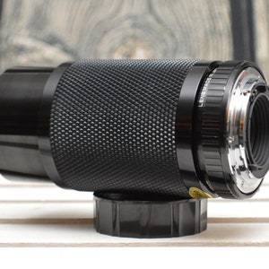 May include: A black camera lens with a silver ring around the front. The lens has a textured surface and the words "Lens Made in Japan" are printed on the side.