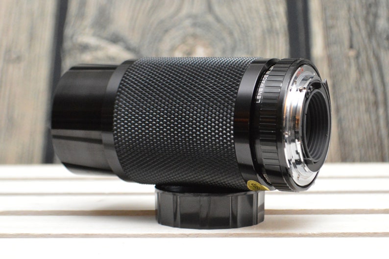 May include: A black camera lens with a silver ring around the front. The lens has a textured surface and the words "Lens Made in Japan" are printed on the side.