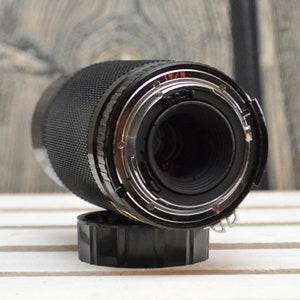 May include: A black camera lens with a silver ring and a black lens cap. The lens is on a white wooden surface.