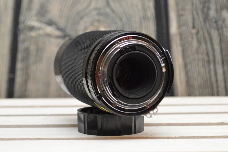 May include: A black camera lens with a silver ring and a black lens cap. The lens is on a white wooden surface.