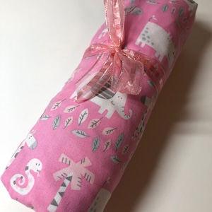 May include: Pink fabric baby blanket with a white ribbon tied around it. The blanket has a pattern of gray and white animals and leaves on a pink background.
