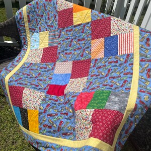 May include: A patchwork quilt with a blue background and various colorful squares. The squares feature different patterns, including stars, stripes, and floral designs. The quilt is edged with a yellow border.
