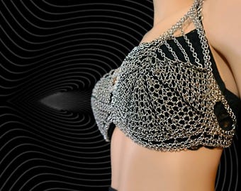 Puede incluir: Un sujetador de malla de cadena plateada con un diseño delicado e intrincado. El sujetador está hecho de pequeños anillos de metal unidos, creando una apariencia de malla. El sujetador lo lleva una persona, pero el foco está en el sujetador en sí.