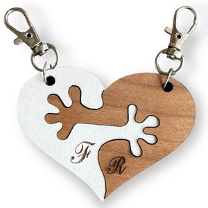 Könnte beinhalten: Ein herzförmiger Schlüsselanhänger aus Holz mit einem Puzzle-Design. Der Schlüsselanhänger ist in zwei Hälften geteilt, jede mit einer anderen Farbe und einem eingravierten Buchstaben. Die linke Hälfte ist weiß mit dem eingravierten Buchstaben "F", und die rechte Hälfte ist braun mit dem eingravierten Buchstaben "R".