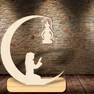 May include: Wooden cutout of a person praying on a crescent moon with a hanging lantern. The cutout is on a wooden base.