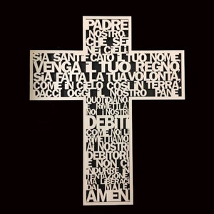 Op de afbeelding: Een wit houten kruis met het Onze Vader in het Italiaans erop geschreven. De woorden zijn uit het hout gesneden, waardoor een decoratief ontwerp ontstaat.