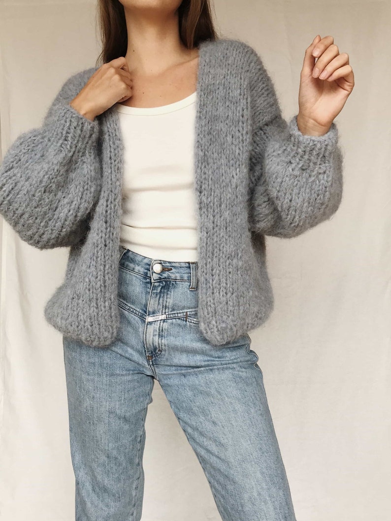 May include: A gray fuzzy cardigan with long sleeves and a relaxed fit. The cardigan is open in the front and has a V-neck.