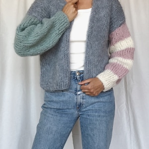 May include: A gray cardigan with a light blue and pink striped sleeve. The cardigan is open in the front and has a v-neck.