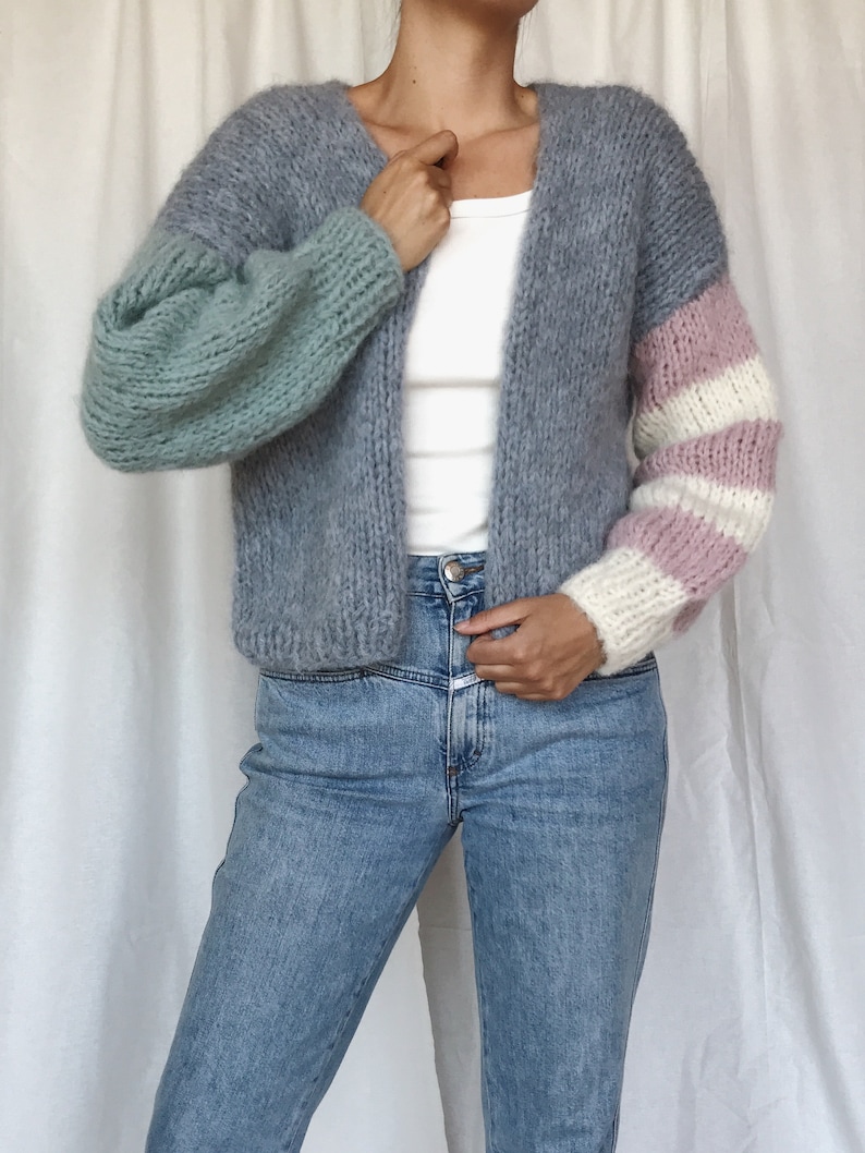 May include: A gray cardigan with a light blue and pink striped sleeve. The cardigan is open in the front and has a v-neck.