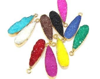 Puede incluir: Una colección de diez colgantes en forma de lágrima con superficies cristalinas texturizadas en colores vibrantes, incluyendo rojo, amarillo, verde, azul, negro, blanco y rosa. Cada colgante está enmarcado en un fino borde de metal dorado con una pequeña argolla.