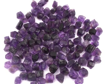 Peut inclure: Un grand tas de cristaux d'améthyste bruts de différentes tailles et formes. Les cristaux sont d'une couleur violette profonde et ont une texture naturelle et rugueuse.