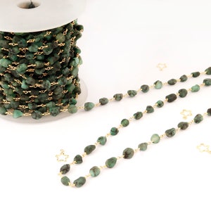 Peut inclure: Une bobine de cha&icirc;ne de pierres pr&eacute;cieuses vert &eacute;meraude avec du fil dor&eacute;. La cha&icirc;ne est compos&eacute;e de petites pierres de forme irr&eacute;guli&egrave;re. Plusieurs brins de la cha&icirc;ne sont dispos&eacute;s, avec des breloques dor&eacute;es en forme d'&eacute;toile.
