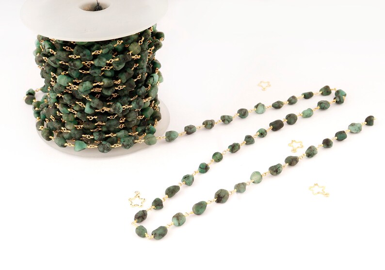 Peut inclure: Une bobine de cha&icirc;ne de pierres pr&eacute;cieuses vert &eacute;meraude avec du fil dor&eacute;. La cha&icirc;ne est compos&eacute;e de petites pierres de forme irr&eacute;guli&egrave;re. Plusieurs brins de la cha&icirc;ne sont dispos&eacute;s, avec des breloques dor&eacute;es en forme d'&eacute;toile.