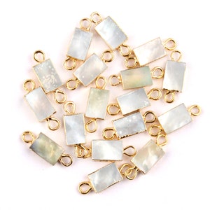 May include: A group of 18 gold-toned metal and white mother-of-pearl rectangular charms with a loop on each end. The charms are scattered on a white surface.