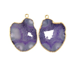 May include: Two purple and white agate stone pendants with gold-coloured edges. Each pendant has a unique shape and a small hole in the centre. The pendants are designed for jewellery making.