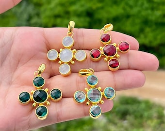 Puede incluir: Cuatro colgantes de cruz dorados con piedras preciosas de colores. Un colgante presenta piedras blancas, otro rojas, un tercero verdes y el último piedras azules y verdes. Cada cruz tiene un lazo dorado para una cadena.