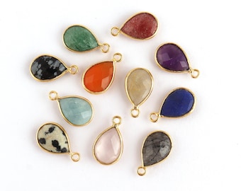 May include: A collection of teardrop-shaped gemstone pendants in various colors, including green, red, orange, and blue. Each stone is set in a gold-colored bezel with a small loop for attaching to a chain or other jewelry component.