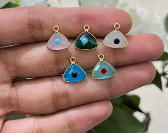 May include: Five triangular charms with gold-toned metal edges, each featuring a central circular stone. The charms include a light pink with turquoise, dark green with turquoise, white with black, bright blue with black, and light green with red.
