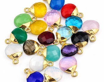 Puede incluir: Una colección de dijes de piedras preciosas facetadas en forma de corazón en varios colores, incluyendo azul, amarillo, verde, rojo, rosa, negro, morado y blanco. Cada dije tiene una tapa de metal dorado con una pequeña argolla circular.
