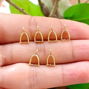May include: Six small gold-toned metal jewelry bails arranged in two rows. Each bail features a U-shaped frame with a small loop at the top for attachment and a horizontal bar at the base, designed for securing pendants or charms to necklaces.