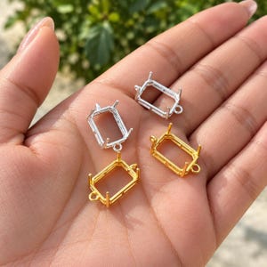 Puede incluir: Cuatro engastes rectangulares de metal para joyería, cada uno con cuatro garras para asegurar piedras preciosas. Dos engastes tienen un acabado en tono plateado brillante y dos tienen un acabado en tono dorado, con una pequeña anilla.