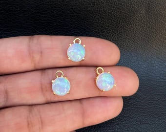 May include: Three gold-toned charms with round, white opal stones. Each charm has a loop at the top for attaching to jewelry.