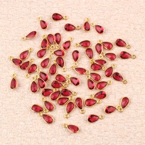 Puede incluir: Una colección de 40 abalorios en forma de lágrima chapados en oro con acentos de cristal rojo. Los abalorios tienen un bucle en la parte superior para sujetarlos a joyas u otras manualidades.