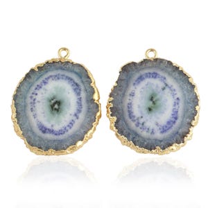 May include: Two round, gold-rimmed agate slices with a white and purple crystal pattern. The slices have a hole at the top for hanging.