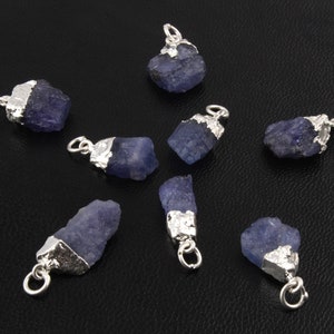 Pode incluir: Oito pingentes de prata com pedras preciosas azuis brutas. Cada pingente tem uma argola de prata para prender a uma corrente ou cordão.