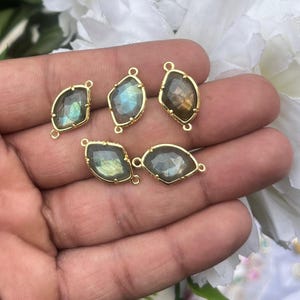 Pode incluir: Cinco pingentes de pedras preciosas com moldura dourada. As pedras preciosas são iridescentes, exibindo tons de azul, verde e castanho. Cada pingente tem um formato irregular único e um pequeno laço.