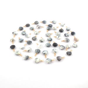 May include: A collection of 40 white and black opal gemstone beads with gold jump rings. The beads are irregularly shaped and have a natural, organic look.