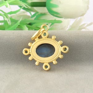 May include: A gold-colored pendant with an oval, dark blue stone at the center. The pendant has a decorative design with small circular accents around the oval stone. A small loop is at the top for a chain.
