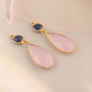 May include: Two gold-tone teardrop-shaped earrings with pink and blue gemstone accents. The earrings have a small round blue gemstone at the top and a larger teardrop-shaped pink gemstone at the bottom.