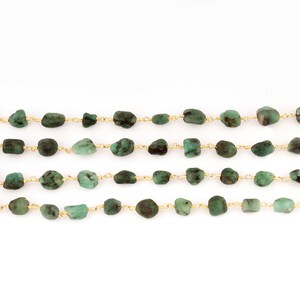 Peut inclure: Quatre rang&eacute;es de pierres pr&eacute;cieuses &eacute;meraude taill&eacute;es &agrave; l'&eacute;tat brut sont enfil&eacute;es sur de fines cha&icirc;nes dor&eacute;es. Les pierres pr&eacute;cieuses varient en taille et en forme, cr&eacute;ant une esth&eacute;tique naturelle. Le fond est blanc.