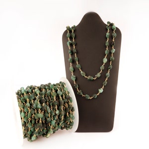 Peut inclure: Un collier et une bobine de perles de pierres pr&eacute;cieuses vert &eacute;meraude avec du fil dor&eacute;. Le collier est pr&eacute;sent&eacute; sur un buste de bijouterie marron fonc&eacute;. Les perles ont une forme irr&eacute;guli&egrave;re et sont enfil&eacute;es.