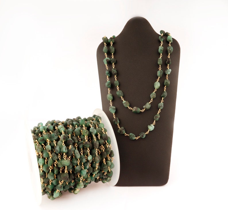 Peut inclure: Un collier et une bobine de perles de pierres pr&eacute;cieuses vert &eacute;meraude avec du fil dor&eacute;. Le collier est pr&eacute;sent&eacute; sur un buste de bijouterie marron fonc&eacute;. Les perles ont une forme irr&eacute;guli&egrave;re et sont enfil&eacute;es.