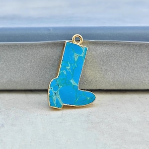 May include: A turquoise and gold-tone boot-shaped pendant. The pendant features a gold-colored border and a bright blue stone with white and green veining. The pendant has a small gold loop at the top for hanging.