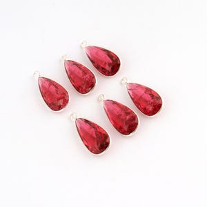 Pode incluir: Seis pingentes em forma de gota com pedras facetadas rosa-escuras em molduras de metal prateado. Cada pingente inclui um pequeno anel circular no topo para fixação, apresentando um corte consistente e uma cor vibrante em todos.