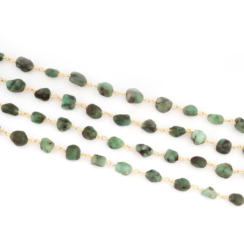 Peut inclure: Quatre rang&eacute;es de perles de pierres pr&eacute;cieuses vert &eacute;meraude sont enfil&eacute;es sur un fil dor&eacute; d&eacute;licat. Les perles sont de forme irr&eacute;guli&egrave;re et varient en nuances de vert, cr&eacute;ant une esth&eacute;tique naturelle. Le fond est blanc.