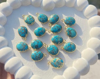 May include: Oval turquoise gemstone pendants with gold-colored metal settings. The turquoise stones have a blue-green hue with brown veining. The pendants are arranged on a white, heart-shaped tray. These pendants are suitable for jewelry making.