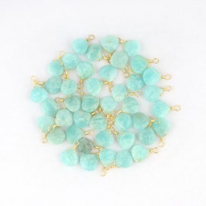 May include: A collection of light blue gemstone pendants with gold-colored wire wrapping. The pendants are heart-shaped and vary slightly in size and shade. The gold wire forms a loop at the top for stringing.