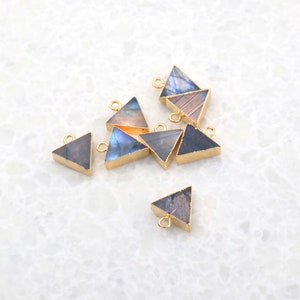 May include: A group of eight gold-plated triangle-shaped pendants with iridescent labradorite stone inlays. The pendants have a loop at the top for attaching to jewelry.